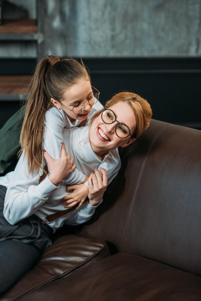 glücklich entzückende Tochter umarmt ihre Mutter von hinten auf der Couch zu Hause - Foto, Bild