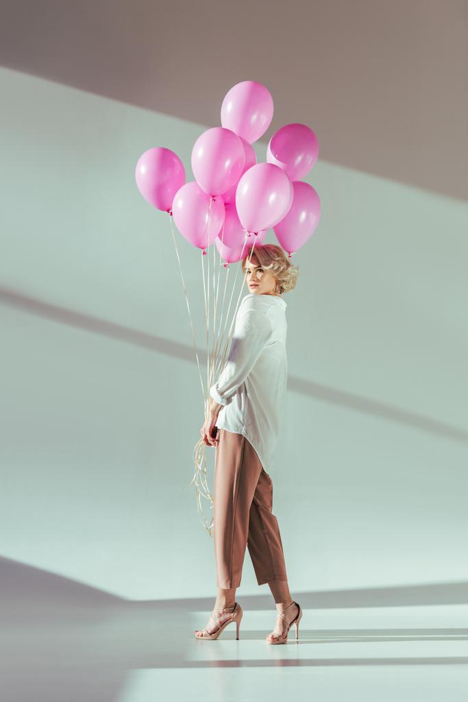 グレーにピンクの風船を持つポーズ ファッショナブルな若いブロンドの女性の完全な長さの表示 - 写真・画像