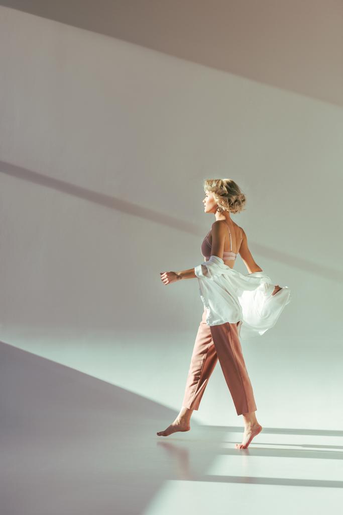 puolella näkymä paljain jaloin blondi tyttö vaaleanpunainen rintaliivit, paita ja housut kävely harmaa
 - Valokuva, kuva