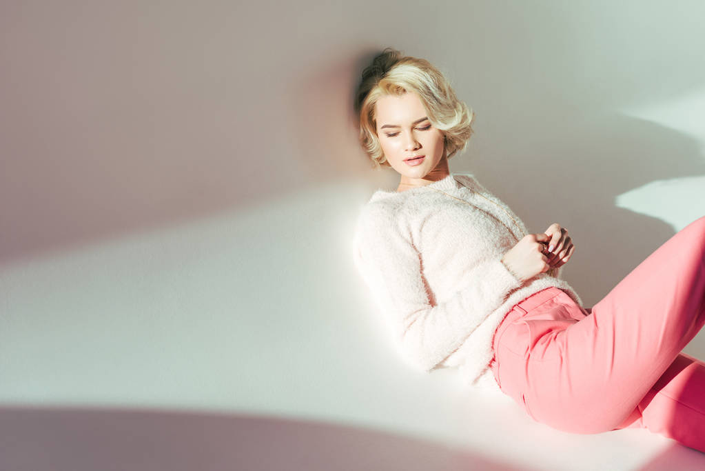 kaunis blondi tyttö vaaleanpunaisissa vaatteissa makaa studiossa harmaa
 - Valokuva, kuva