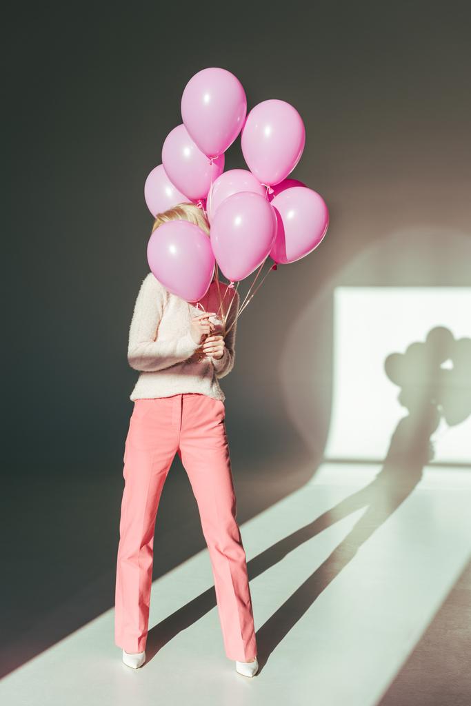 Δείτε πλήρες μήκος κομψό νεαρή γυναίκα που ποζάρει με ροζ μπαλόνια στο studio  - Φωτογραφία, εικόνα
