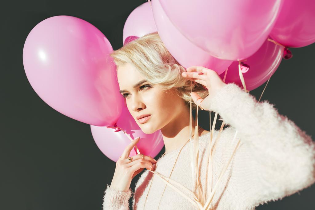 hermosa mujer joven sosteniendo globos rosados y mirando hacia otro lado aislado en gris
 - Foto, imagen