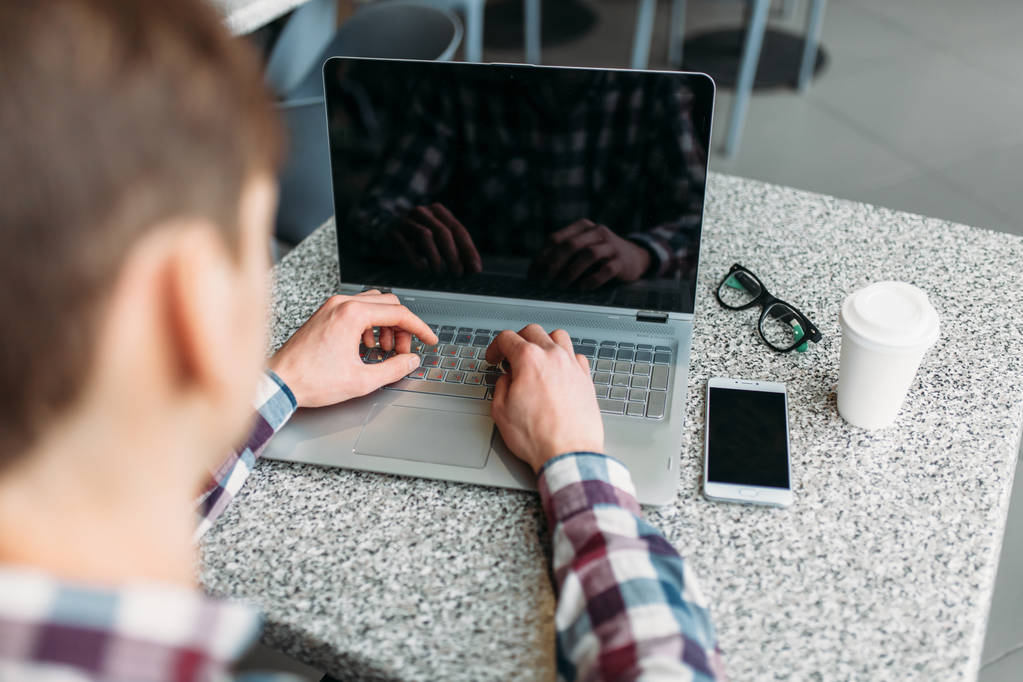 Um homem senta-se em um café e trabalhando em laptop, à procura de trabalho, o estudante escreve o dever de casa, um cara de camisa e óculos
 - Foto, Imagem