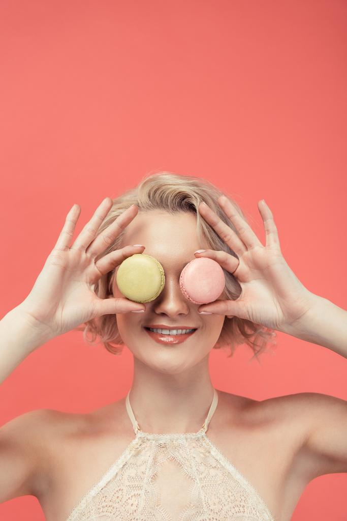 mooie lachende vrouw met twee macarons in front of eyes, geïsoleerd op rood - Foto, afbeelding