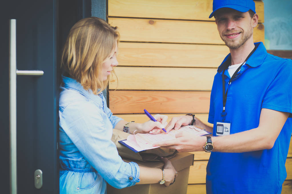 Lächelnder Zusteller in blauer Uniform liefert Paketkasten an Empfänger aus - Kurierdienst-Konzept. Lächelnder Zusteller in blauer Uniform - Foto, Bild