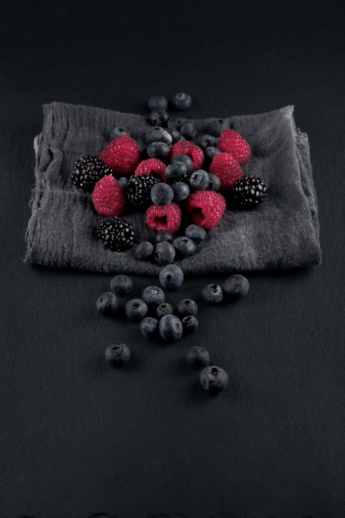 fresh ripe blueberries, blackberries and raspberries on a napkin and slate plate kitchen table can be used as background - Photo, Image