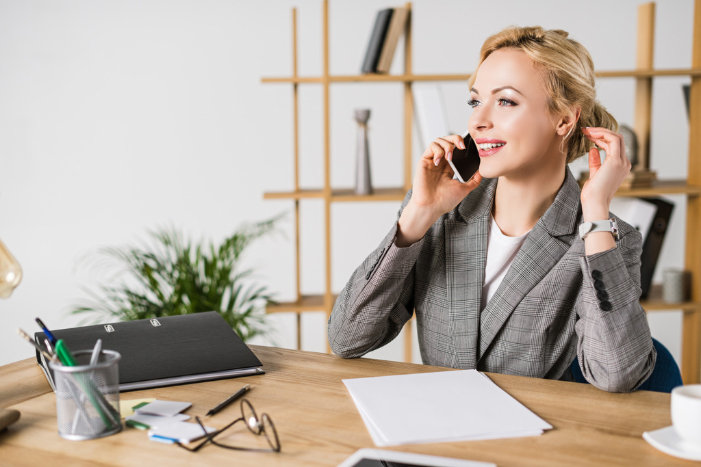 mujer de negocios sonriente hablando en el teléfono inteligente en el lugar de trabajo en la oficina
 - Foto, imagen