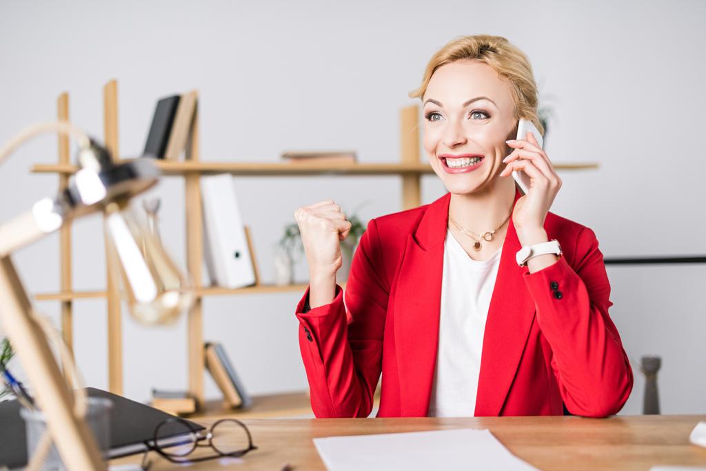 portrait of excited businesswoman talking on smartphone at workplace in office - Photo, Image