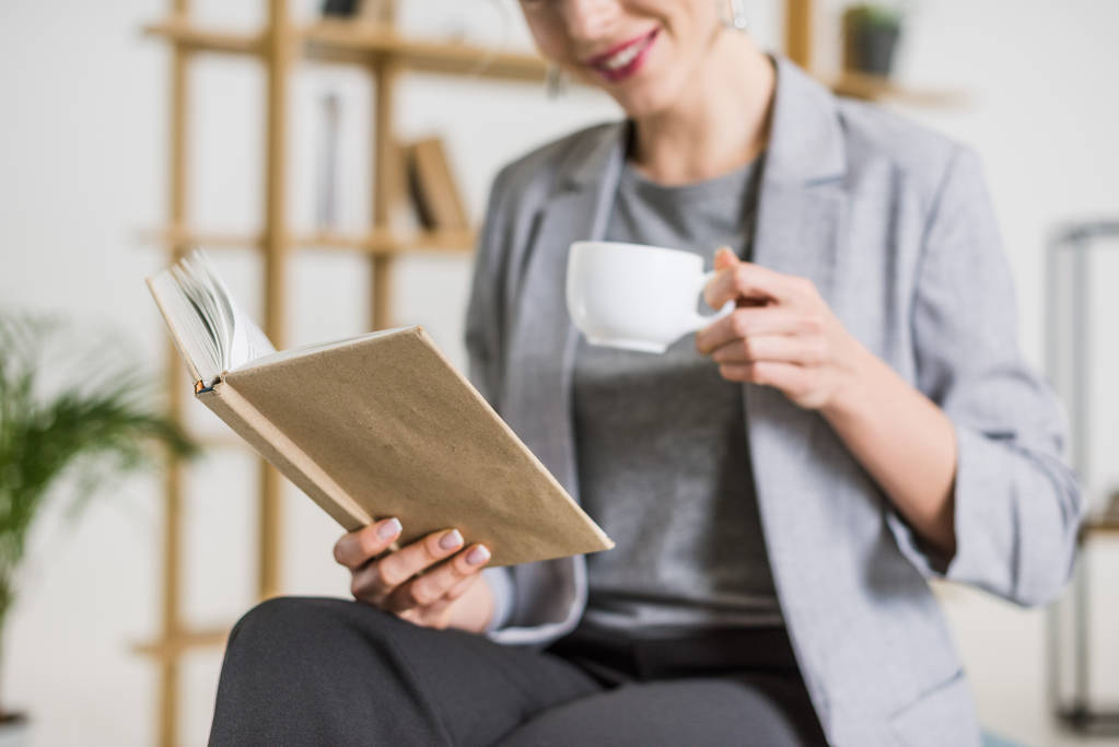 tiro recortado de mulher de negócios sorridente com livro e xícara de café
 - Foto, Imagem