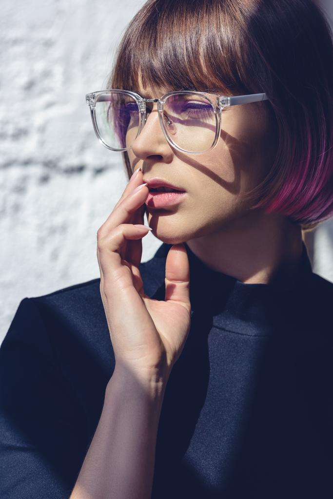 mooie stijlvolle vrouw met roze haren en glazen aanraken van de lippen met hand - Foto, afbeelding