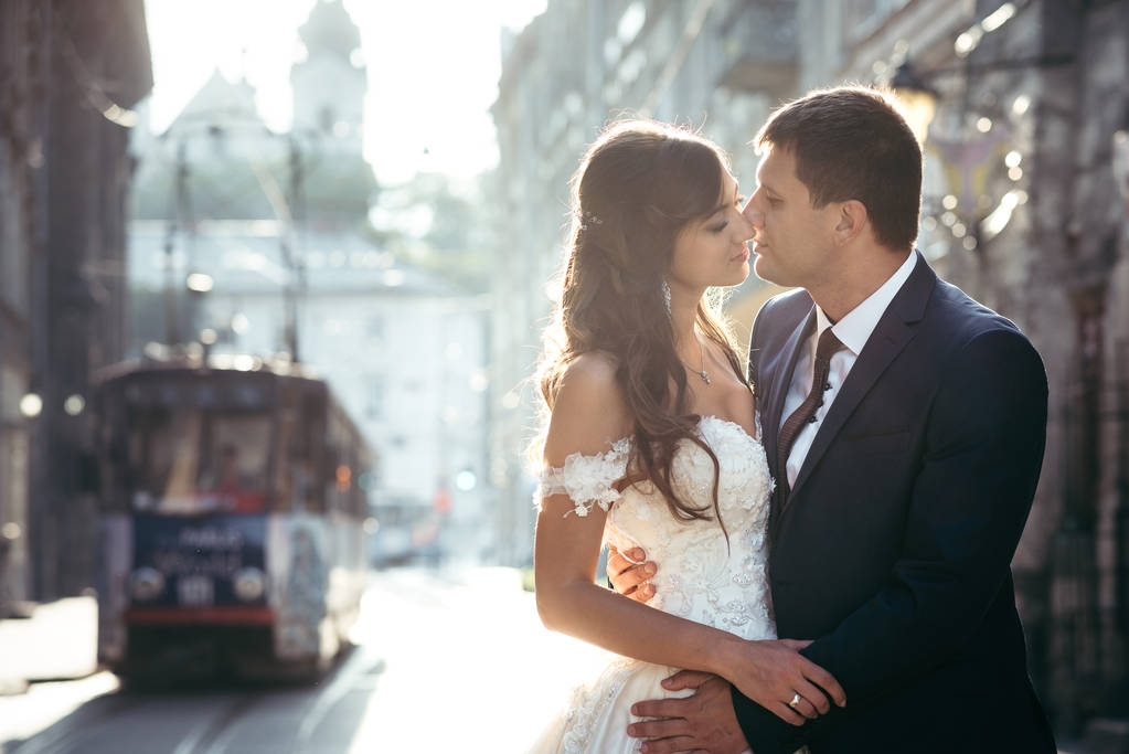 Retrato romántico de cerca de los atractivos recién casados abrazándose al fondo de la vieja ciudad durante la puesta del sol
. - Foto, Imagen