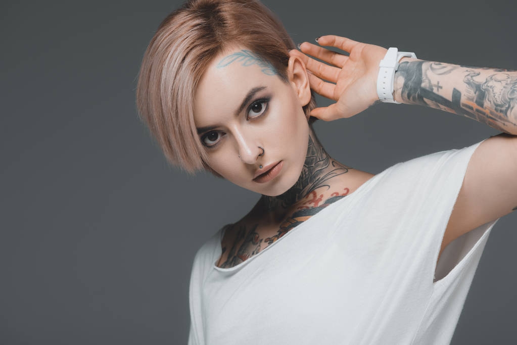 portrait of attractive tattooed girl in white t-shirt looking at camera isolated on grey - Photo, Image