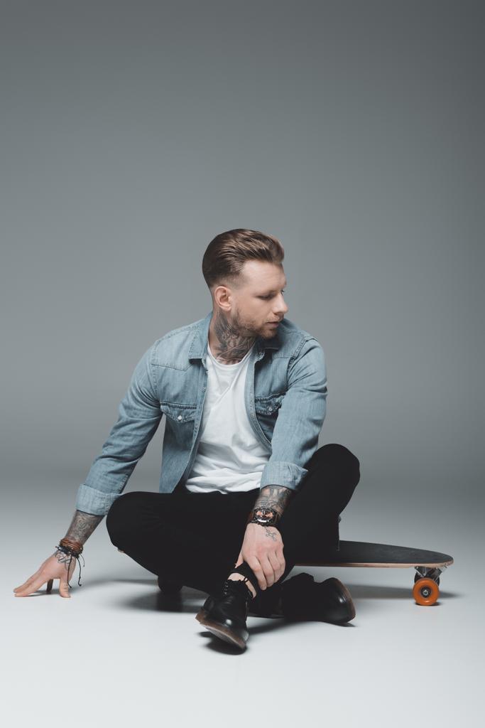 pěkný elegantní mladý muž sedí na skateboard a koukal na grey - Fotografie, Obrázek