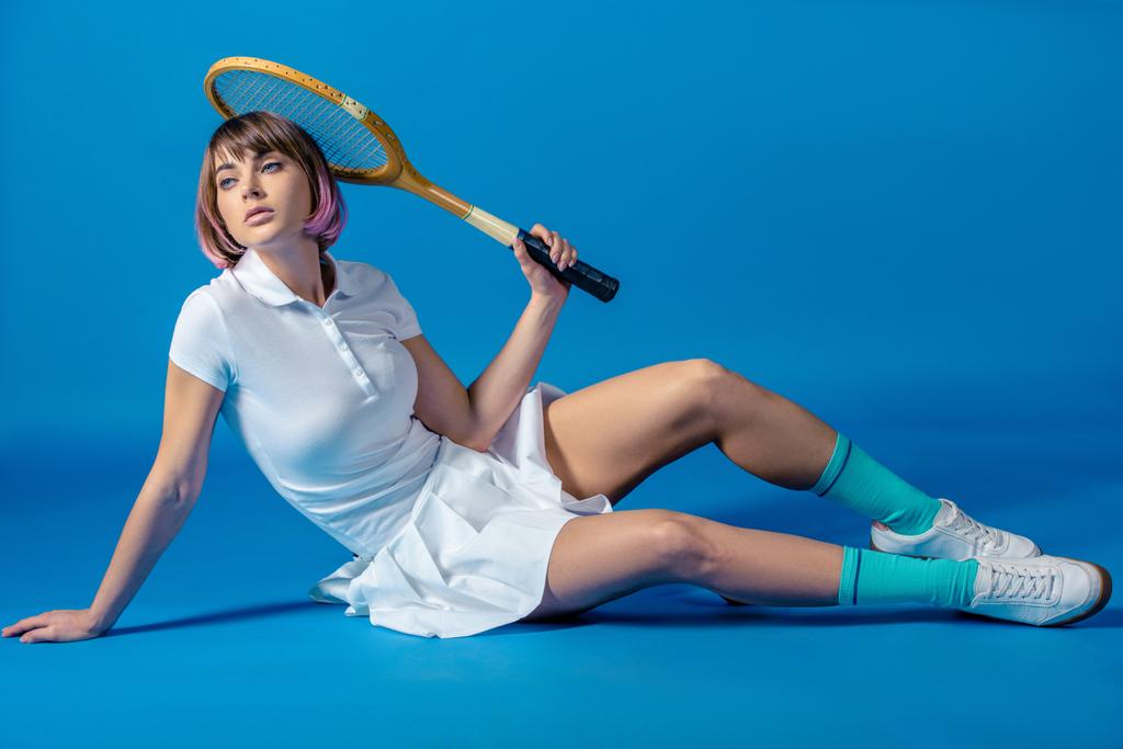 sexy Tennis player sitting with tennis racket and looking away on blue - Photo, Image