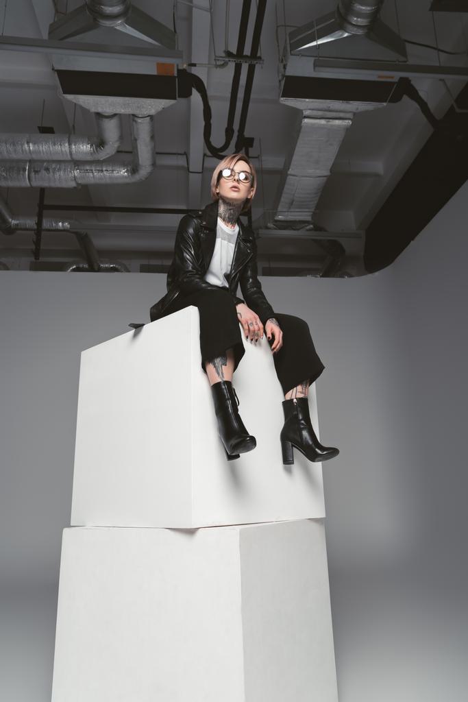 vue à angle bas de la jeune femme tatouée élégante assise sur des cubes blancs en studio
 - Photo, image