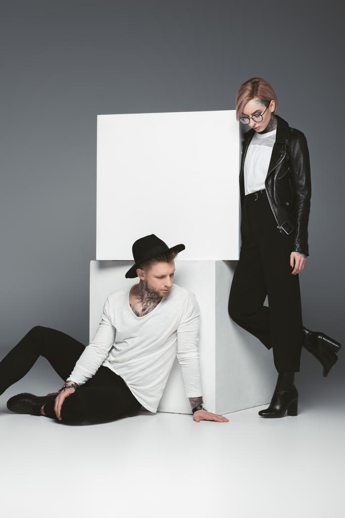 stylish tattooed couple posing near white cubes, isolated on grey - Photo, Image