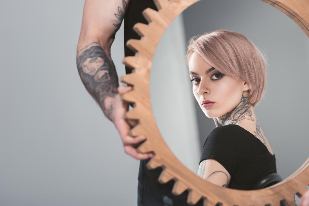 tattooed man holding mirror with reflection of his beautiful girlfriend, isolated on grey - Photo, Image