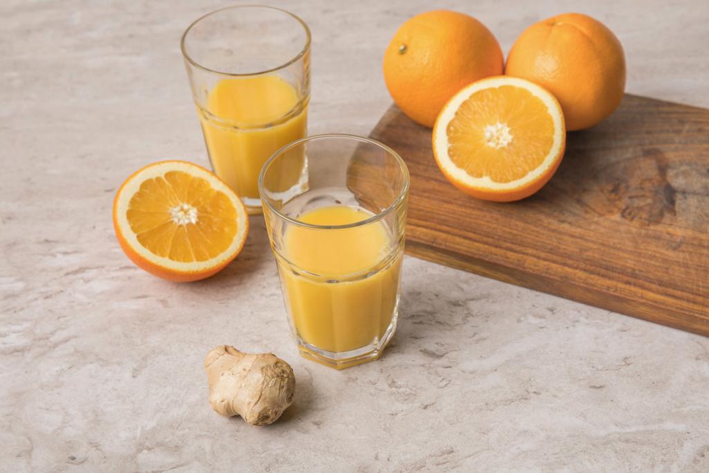 hoge hoekmening van zelfgemaakte jus d'orange en sinaasappelen met gember op marmeren tafel - Foto, afbeelding