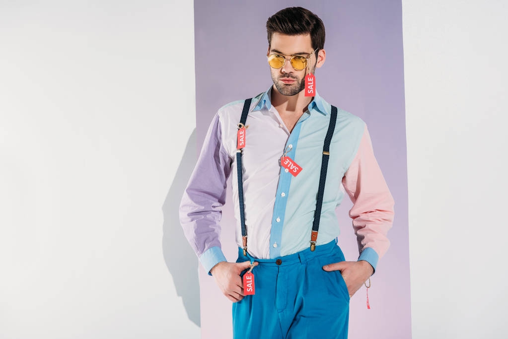 schöner, stylischer junger Mann mit Sonnenbrille und Verkaufsetiketten auf grau - Foto, Bild