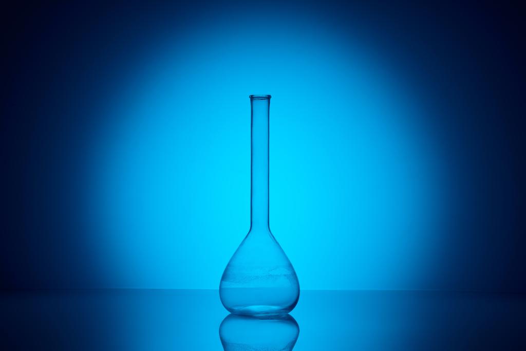 un matraz de vidrio transparente sobre mesa reflectante en laboratorio sobre azul
 - Foto, imagen