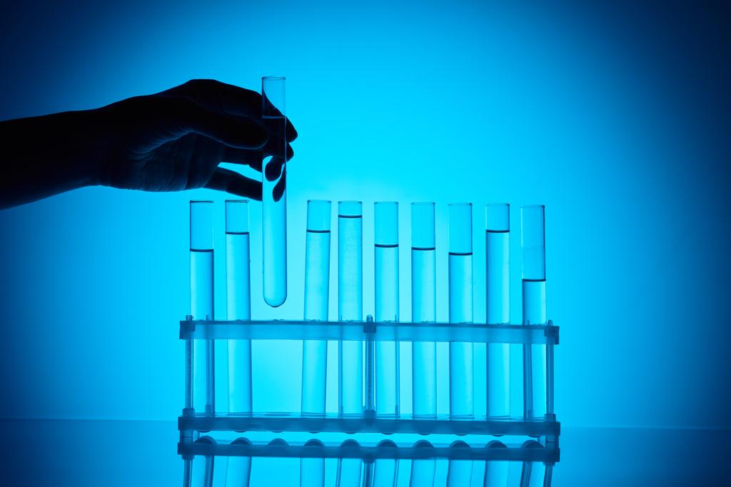 cropped image of female chemist taking glass tube from stand on blue - Photo, Image