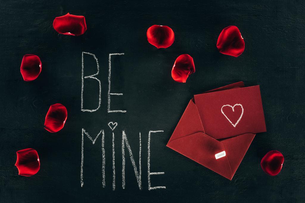 literowanie Be Mine pośród płatków róży i czerwoną kopertę na czarnej powierzchni - Zdjęcie, obraz