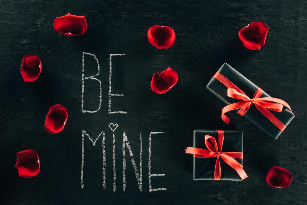 lettering BE MINE surrounded with rose petals and gift boxes on black surface - Photo, Image
