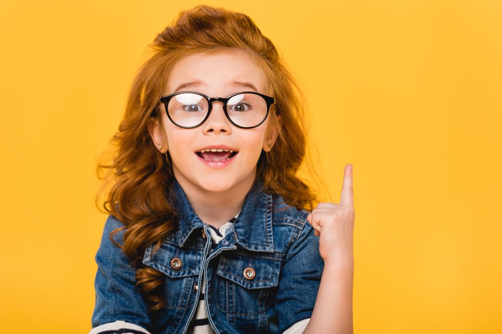 portrait of smiling little kid in eyeglasses pointing up isolated on yellow - Photo, Image