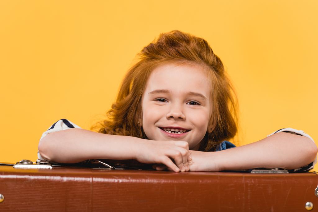 portrait of smiling kid leaning on suitcase isolated on yellow - Photo, Image