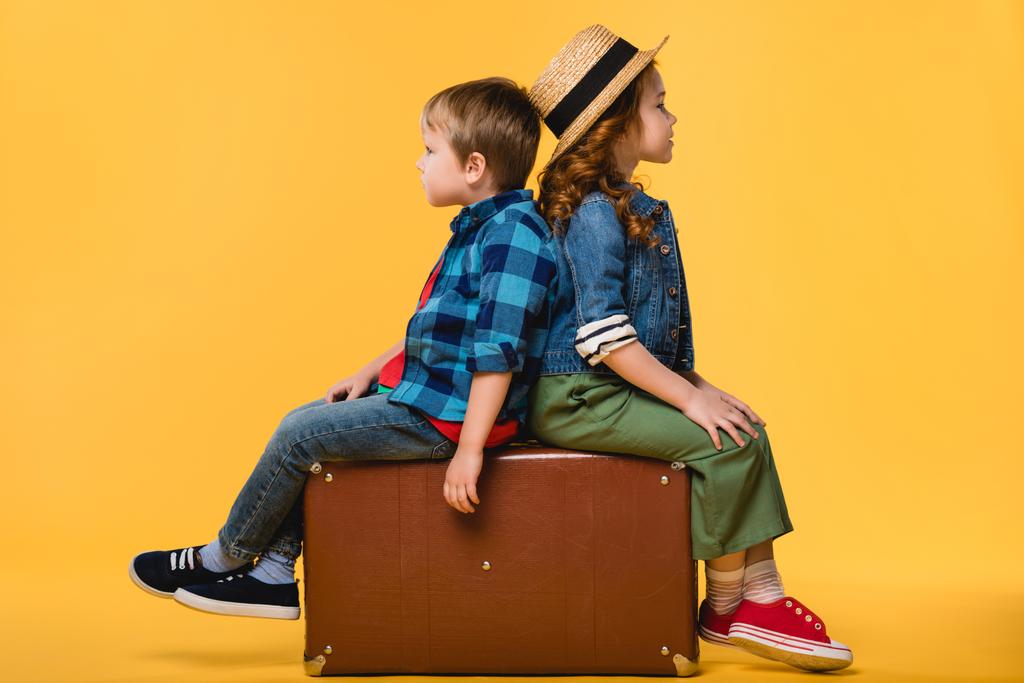 vue latérale des enfants assis sur une valise en cuir isolée sur du jaune
 - Photo, image