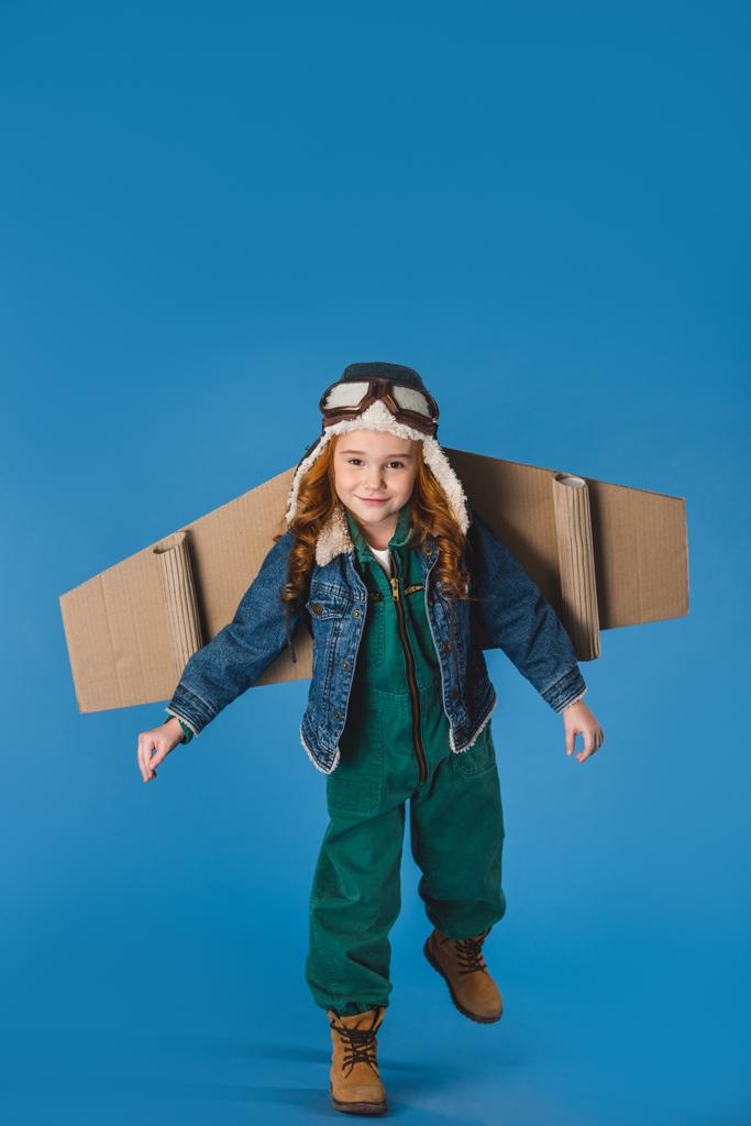 adorable preteen kid in pilot costume with paper plane wings isolated on blue - Photo, Image