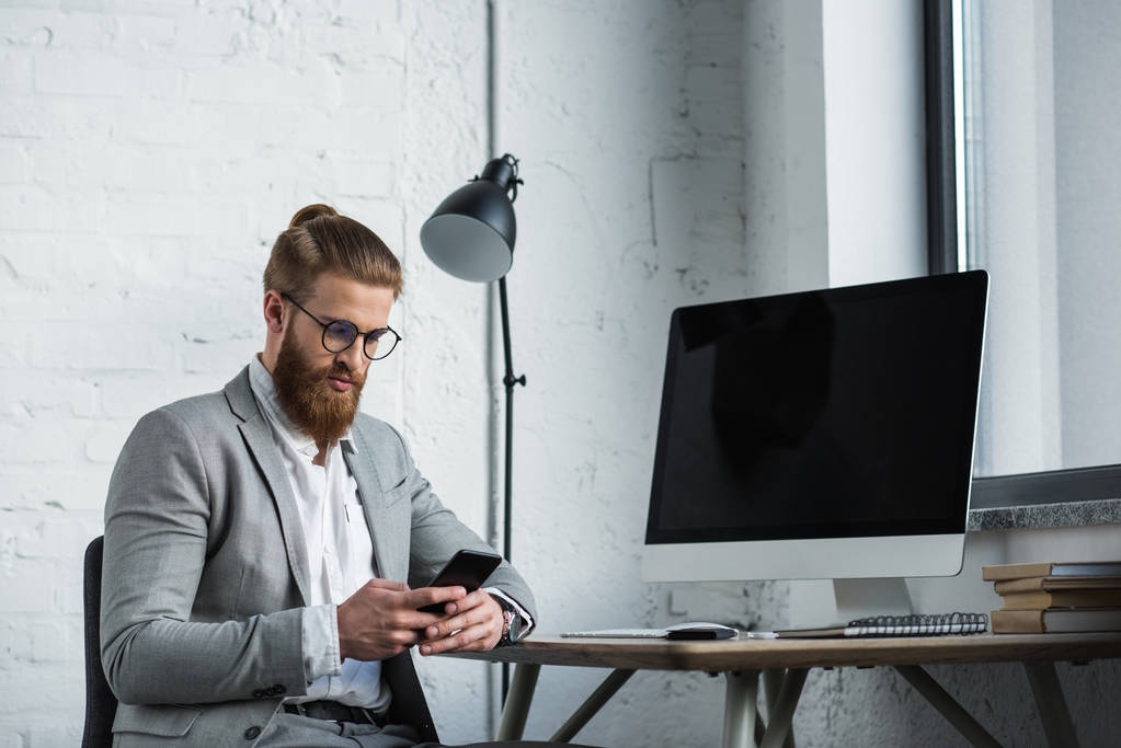 красивый бородатый бизнесмен смотрит на смартфон в офисе
 - Фото, изображение