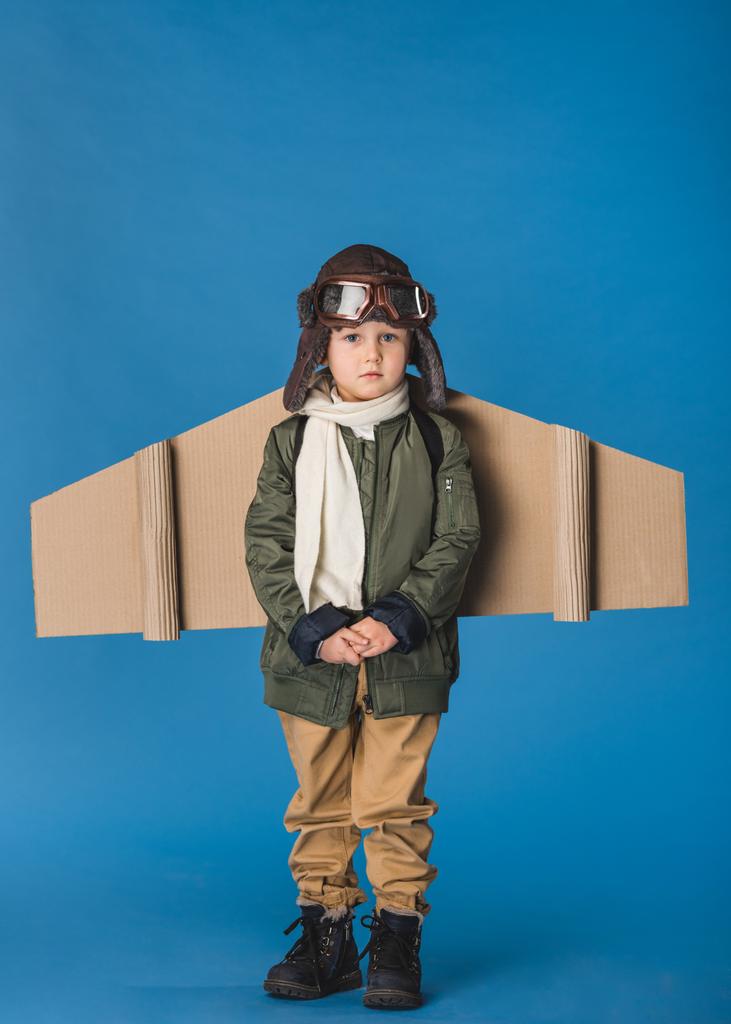 cute little boy in pilot costume with paper plane wing isolated on blue - Photo, Image