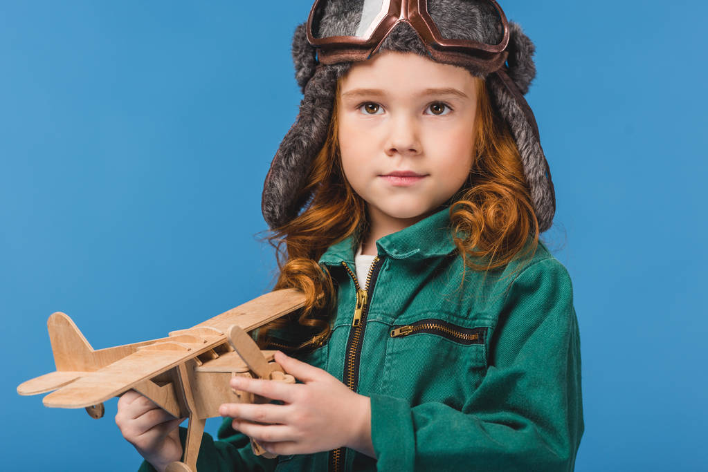 portrait of adorable child in pilot costume with wooden plane toy isolated on blue - Photo, Image