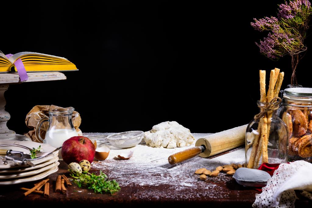 vue rapprochée de la pâte, du rouleau à pâtisserie, de la branche sèche et de la cruche en verre avec lait noir
  - Photo, image