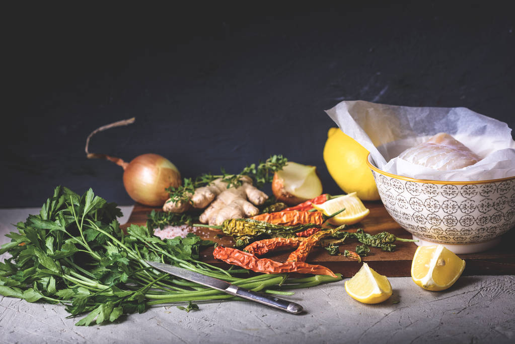 vista de cerca del pescado crudo en un tazón, perejil, pimientos, sal, cebolla, limón y jengibre en una tabla de cortar de madera
  - Foto, imagen