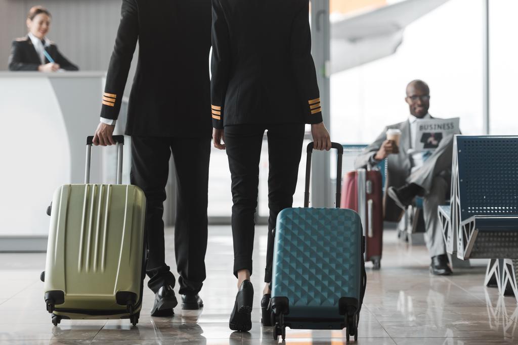 スーツケースを空港のロビーで歩いている男性と女性パイロットのショットをトリミング - 写真・画像
