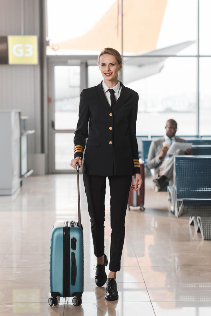 Gelukkig vrouwelijke piloot met koffer wandelen door luchthaven lobby - Foto, afbeelding