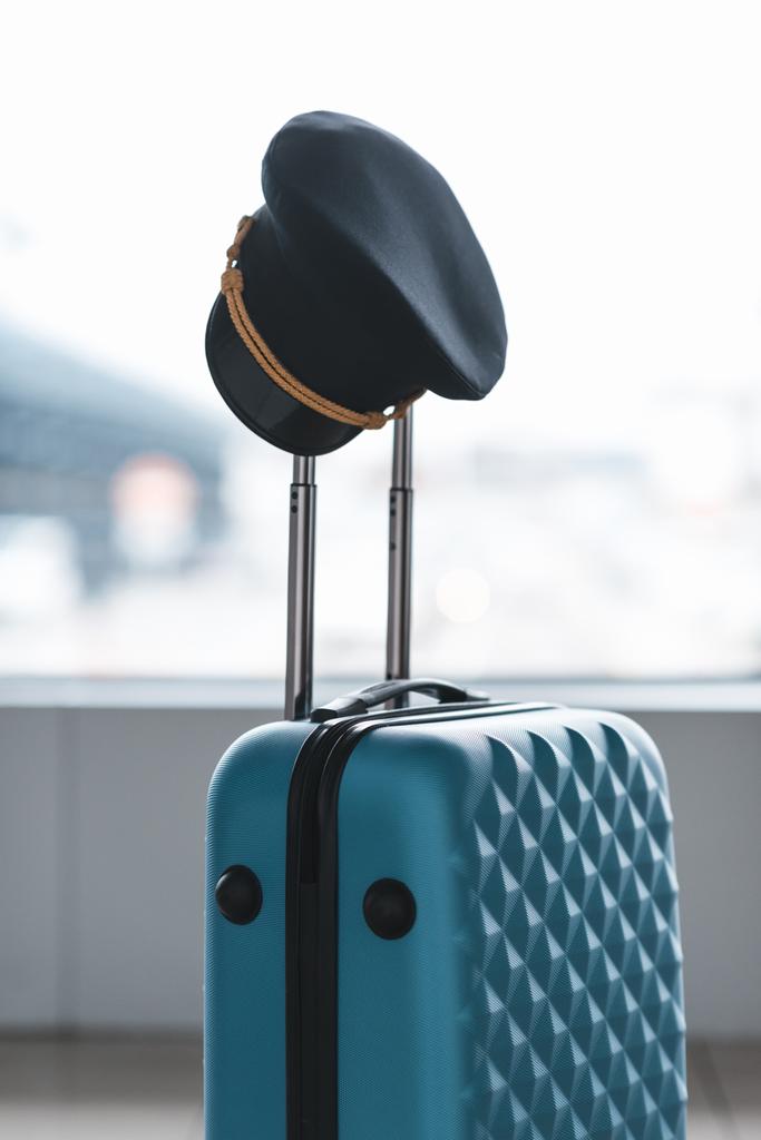 Pilotenmütze hängt am Griff des Koffers am Flughafen - Foto, Bild