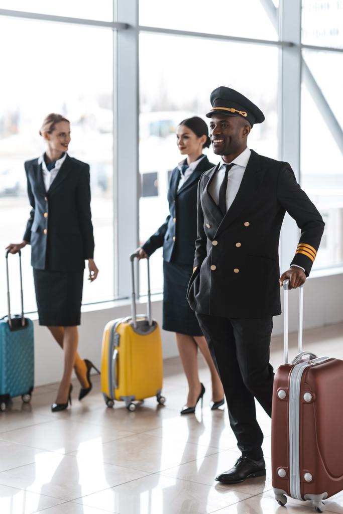 νεαρός πιλότος και αεροσυνοδοί με αποσκευές με τα πόδια από το αεροδρόμιο - Φωτογραφία, εικόνα