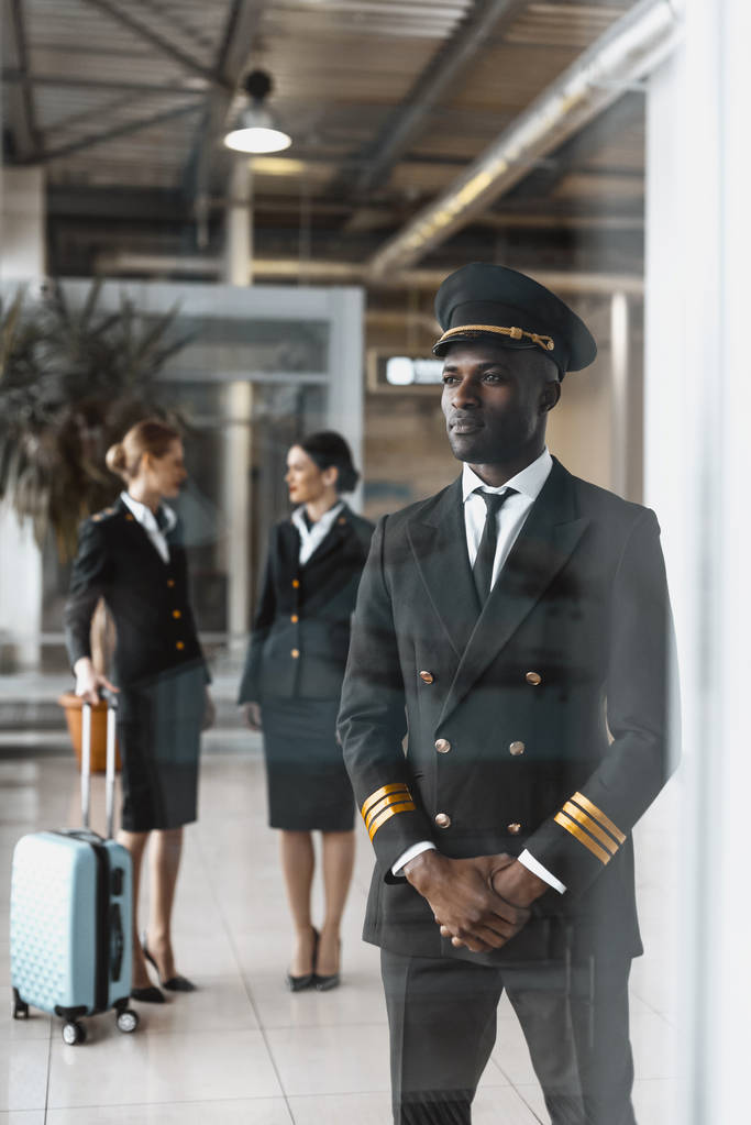 knappe jonge piloot in luchthaven met stewardessen voor vlucht - Foto, afbeelding