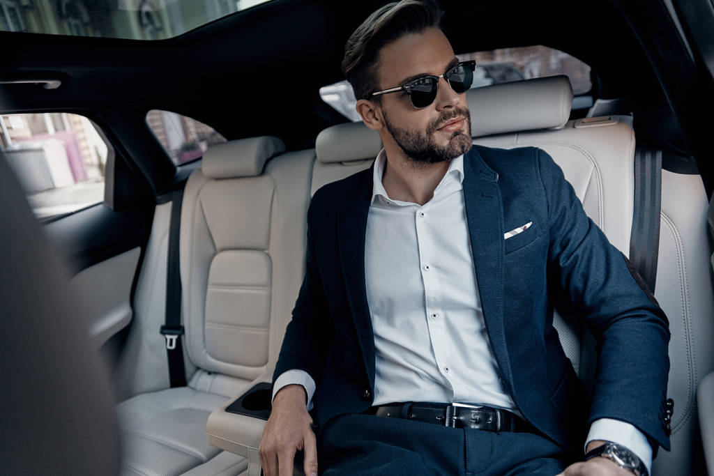 Hombre joven guapo en traje y gafas mirando hacia otro lado mientras está sentado en el coche
 - Foto, imagen