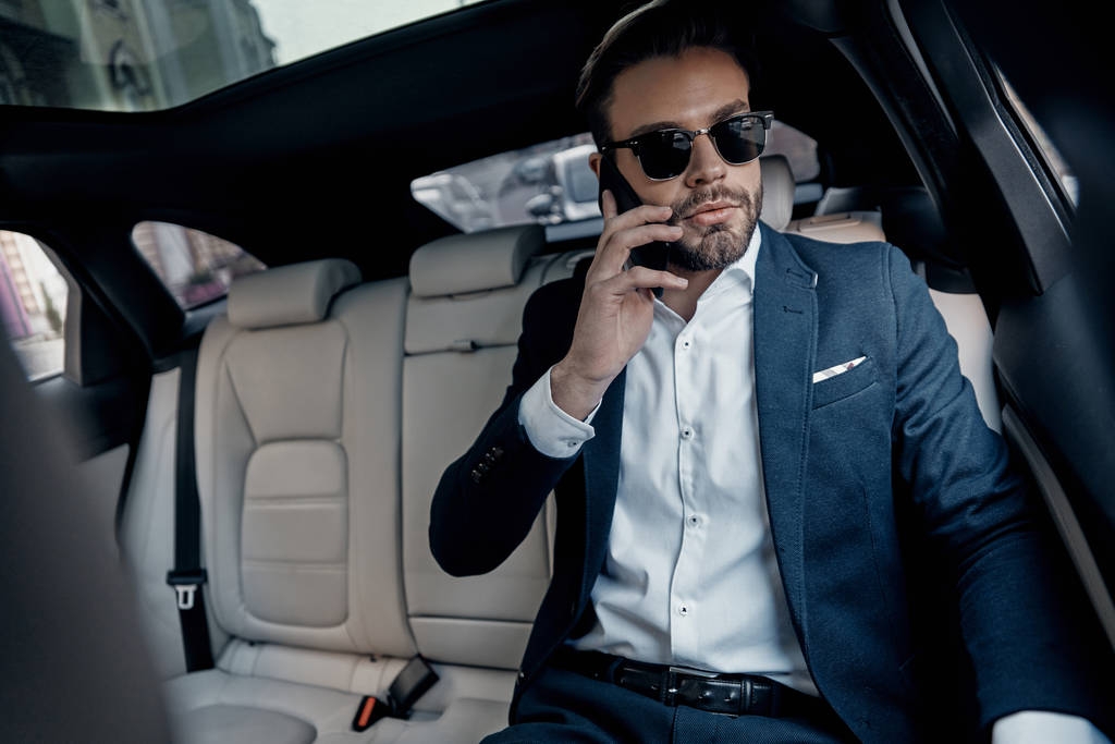 Przystojny, młody człowiek w garnitur dyskusji biznesowych szczegóły na telefon siedząc w samochodzie - Zdjęcie, obraz