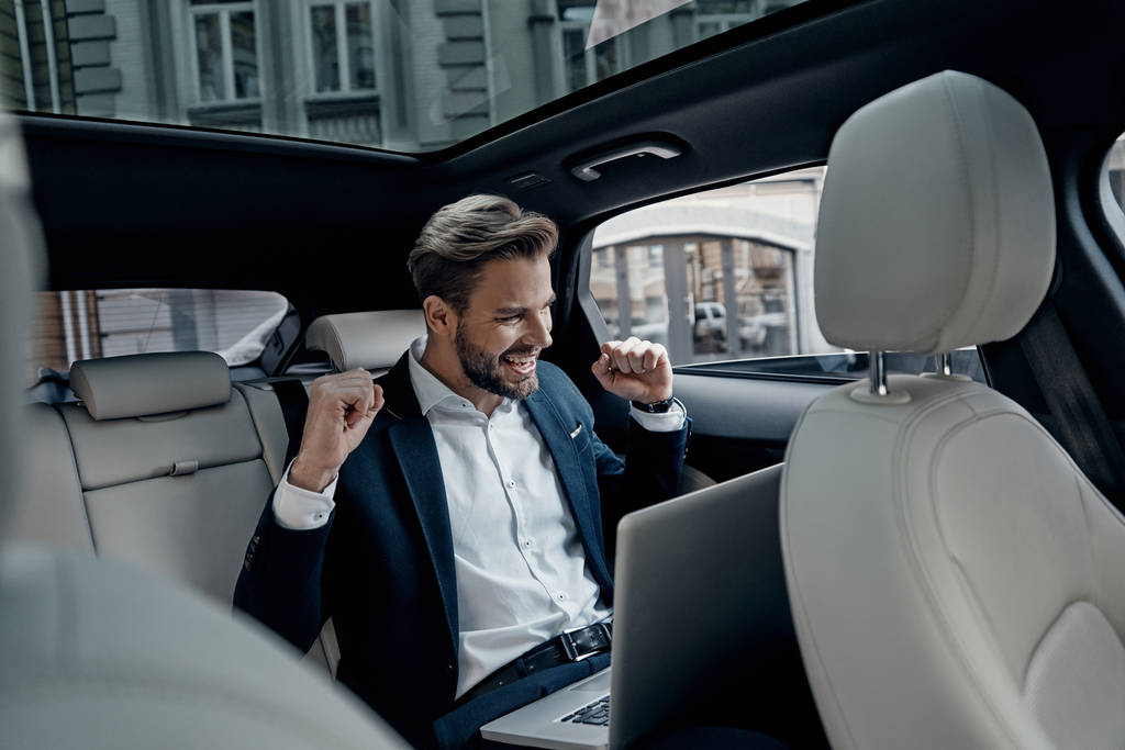 homem de negócios feliz em terno sorrindo de sucesso enquanto sentado no carro com laptop
 - Foto, Imagem