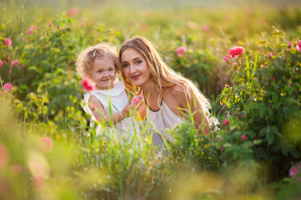 Beautiful couple child girl with pretty young mother are walking in spring garden with pink blossom roses flowers - Photo, Image