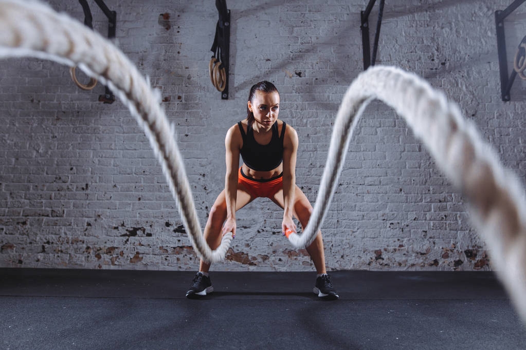 Jovem mulher trabalhando com cordas de batalha em cross fit ginásio
 - Foto, Imagem