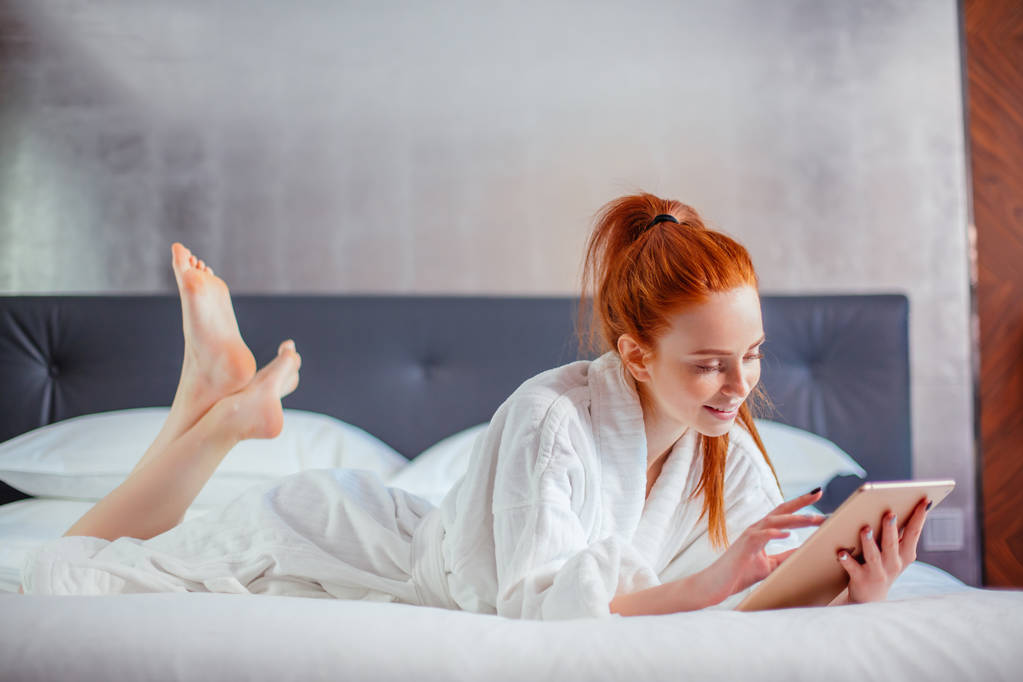 hermosa mujer con albornoz y el uso de tabletas digitales mientras se relaja en la cama
 - Foto, imagen