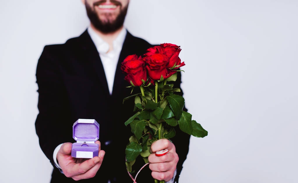 Bude moje žena. Elegantní krásná usmívající se muž s červenými růžemi a snubní prsten v krabici na bílém pozadí. - Fotografie, Obrázek
