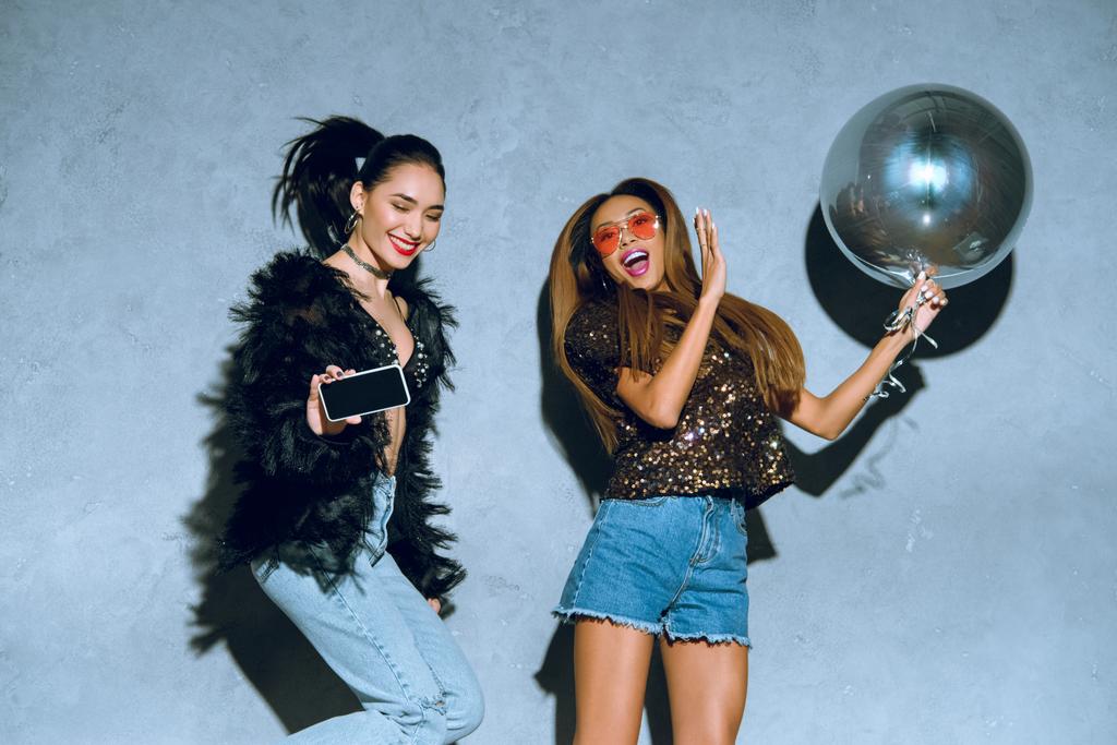 donne multietniche alla moda con smartphone e palloncino che si divertono insieme alla festa
 - Foto, immagini