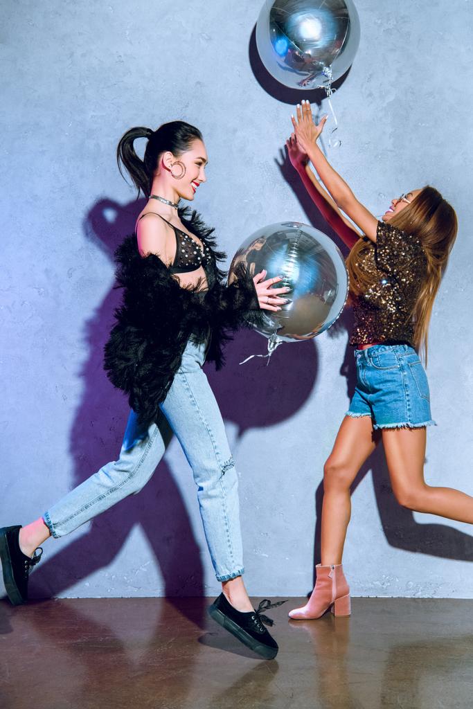 вид сбоку на счастливых стильных многоэтнических женщин, веселящихся с серебряными воздушными шарами
 - Фото, изображение